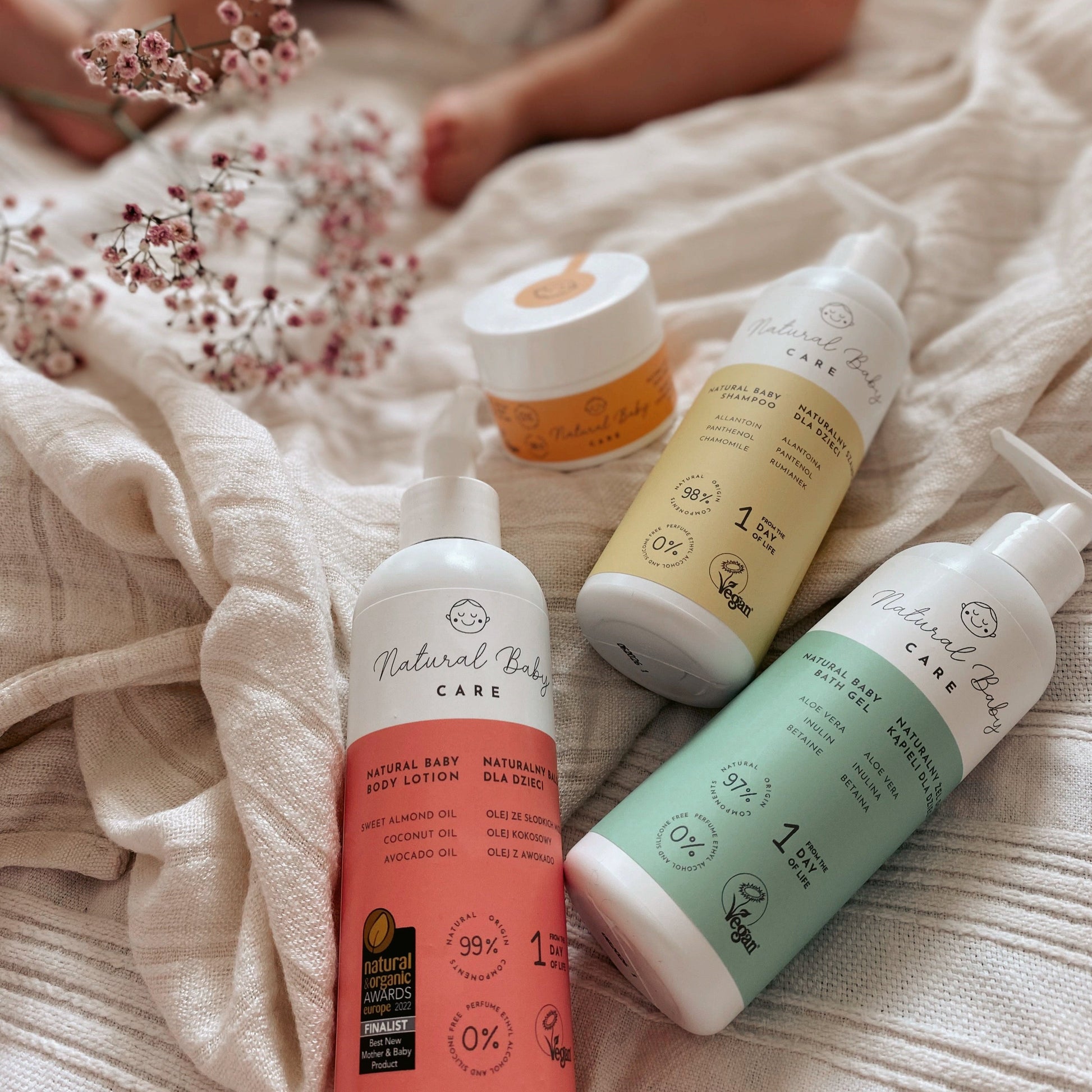 Naturalny krem do twarzy dla dzieci oraz inne produkty Natural Baby Care na tle tkaniny i kwiatów.